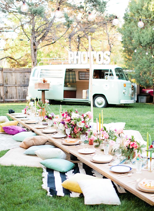 a picnic table set up outside with food and drinks on it, along with an old vw camper in the background