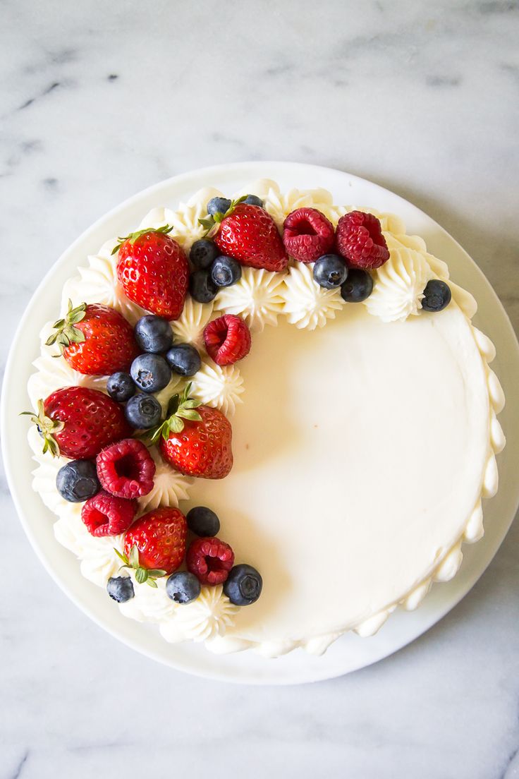 a white cake with strawberries, blueberries and raspberries arranged in the shape of a wreath