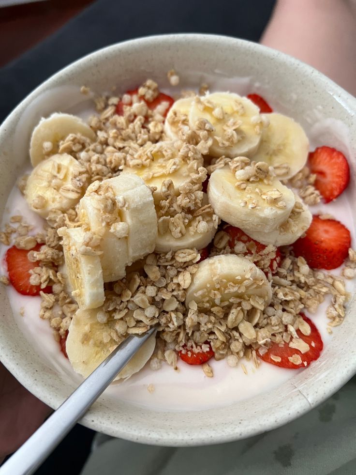 a white bowl filled with granola, strawberries and sliced banana's on top