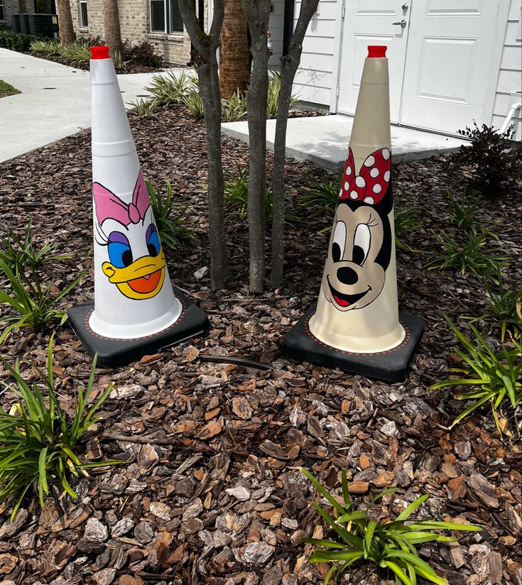 two plastic cone shaped like cartoon characters sitting on top of mulch next to a tree