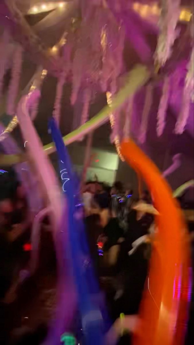 blurry photograph of people dancing with colored streamers in the air at a party