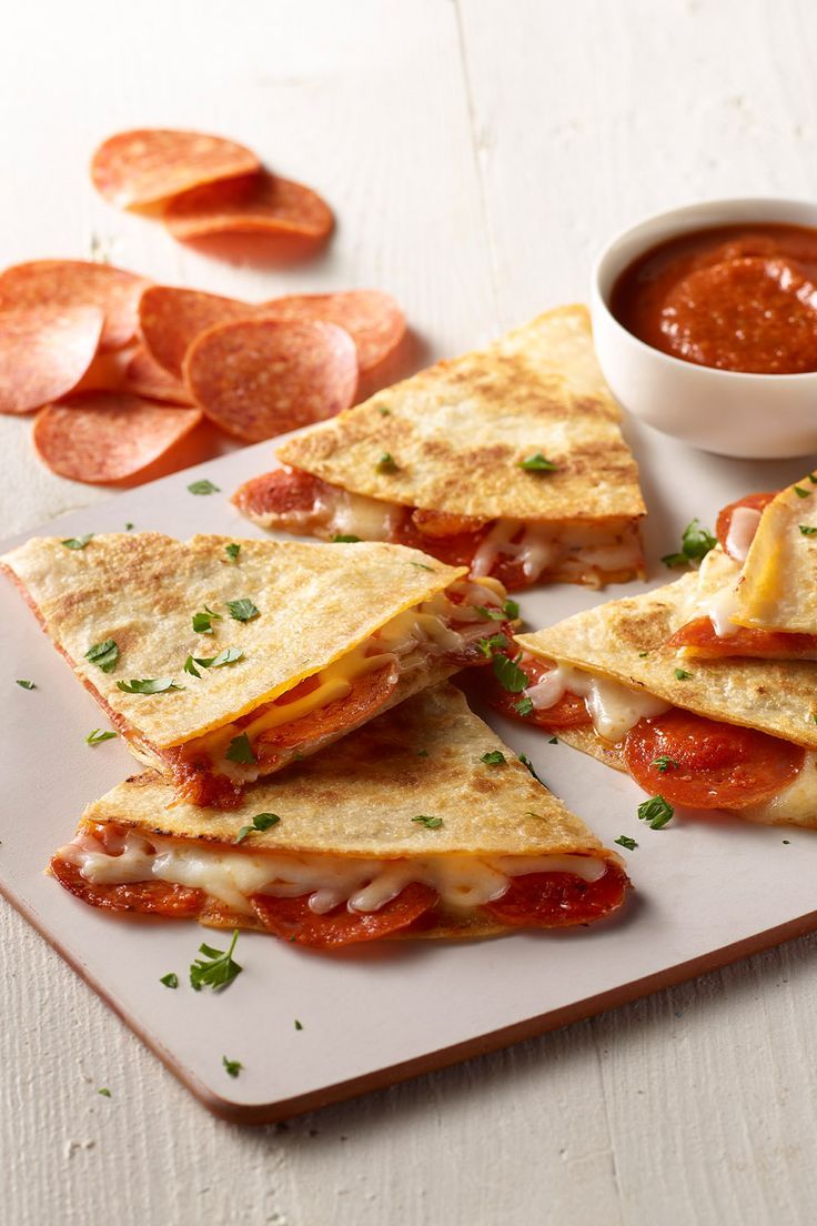 several quesadillas on a white plate with sauce and pepperoni slices next to it