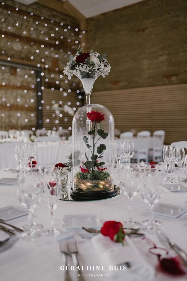 the table is set with wine glasses, silverware and roses in a glass dome