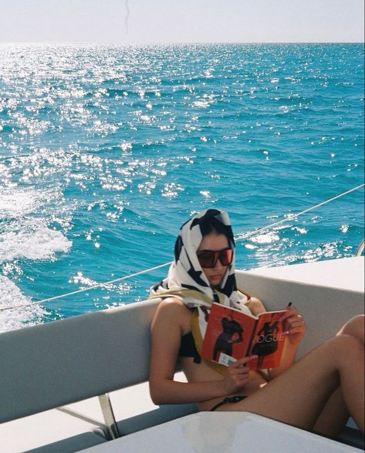 a woman sitting on the back of a boat while reading a book in her lap