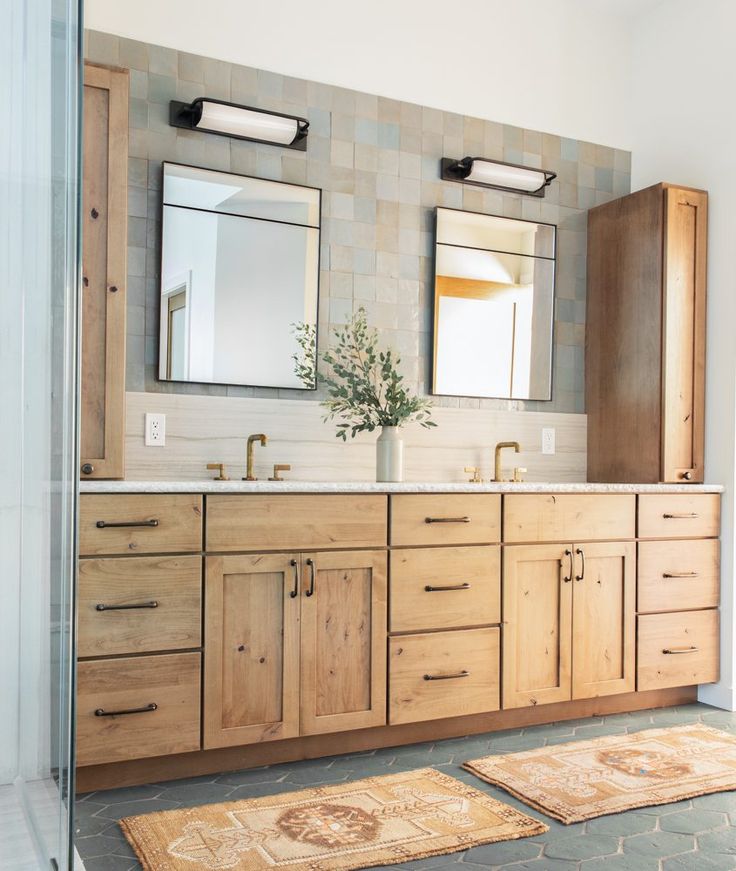 a bathroom with two sinks and mirrors on the wall next to rugs in front of it