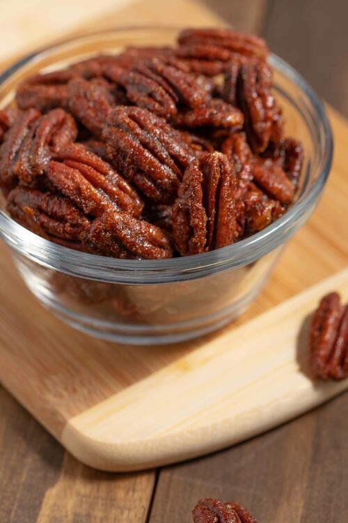 a glass bowl filled with pecans sitting on top of a wooden cutting board