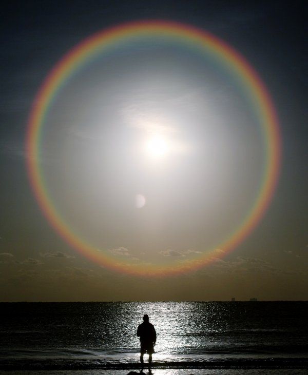 a man standing on top of a beach under a rainbow ring