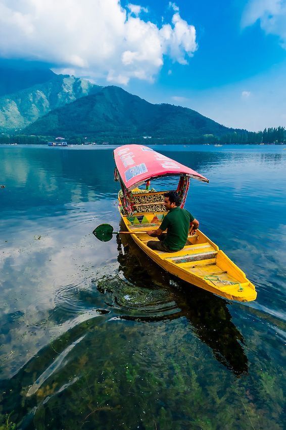 a man sitting in a yellow boat on top of a body of water with mountains in the background