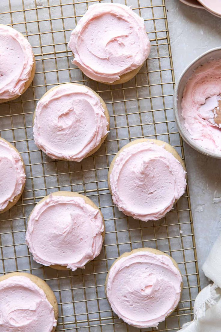 pink frosted cookies are on a cooling rack next to a bowl of whipped cream