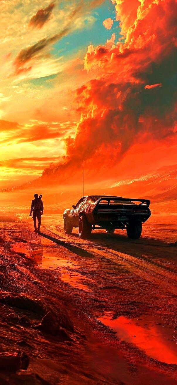 two people walking on the beach next to an old car in front of a sunset