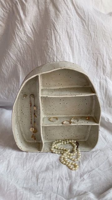 an empty white purse with pearls and necklaces on the bottom, sitting on a bed