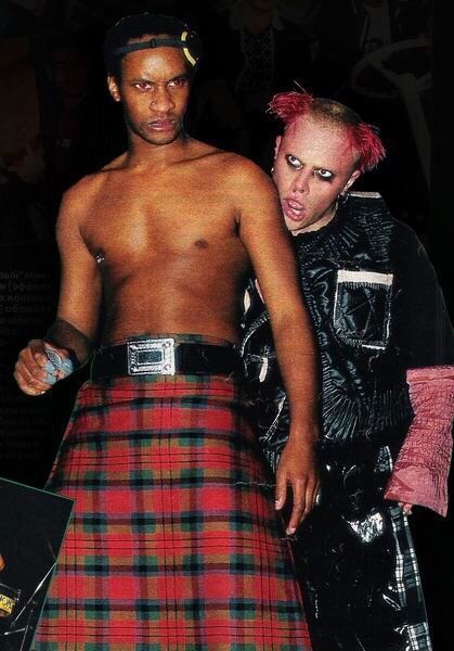 a man in a kilt walking next to a woman with pink hair and piercings