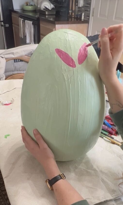 a woman is painting an egg with pink paint