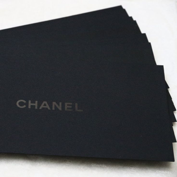 black paper with the word chanel written on it in silver lettering, placed on a white surface