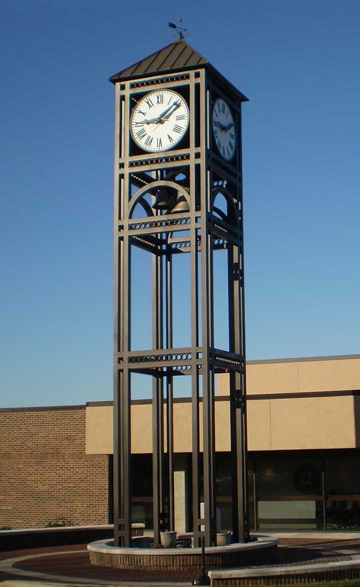 a large metal clock tower sitting in front of a building with a clock on it's side