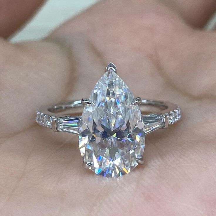 a woman's hand holding an engagement ring with a pear shaped diamond in the center