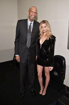 a man and woman standing next to each other in front of a wall with pictures on it