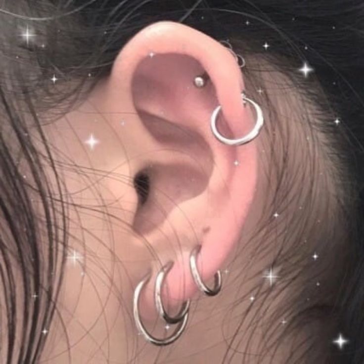 a close up of a person's ear with silver hoops