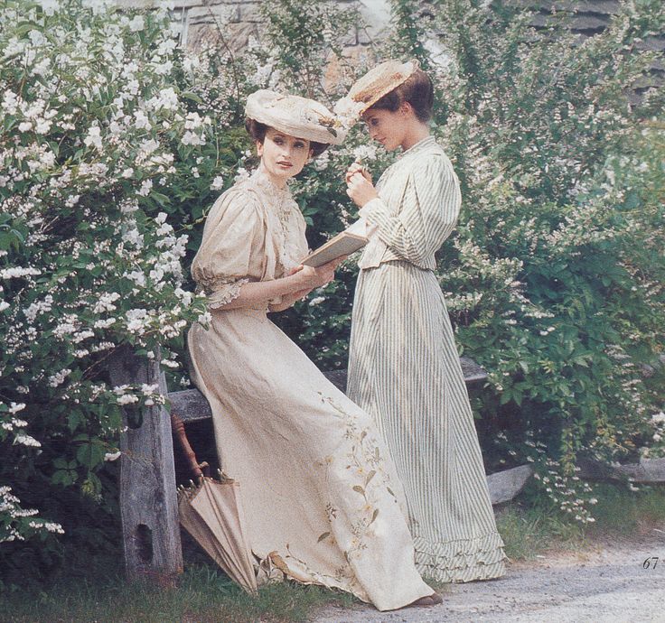 two women standing next to each other in front of some bushes and white flowers on a sunny day