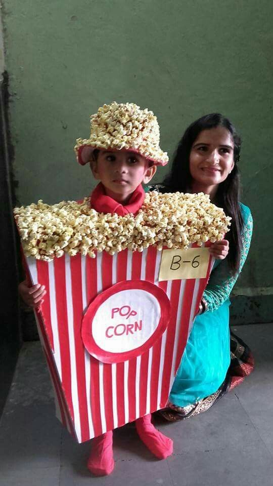 two children wearing popcorn costumes and one is holding up a sign that says pop corn