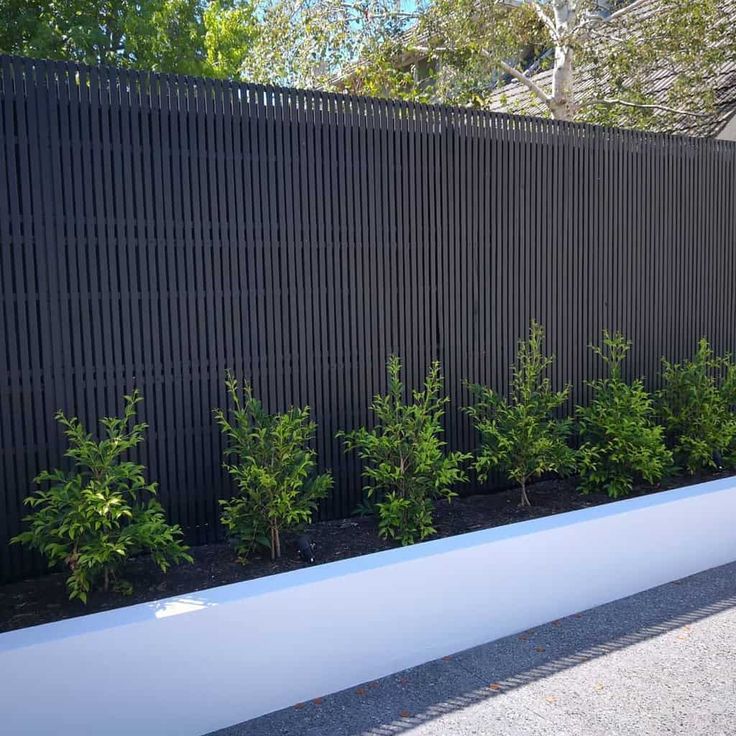 a black fence with white planters in front of it and some green plants on the side