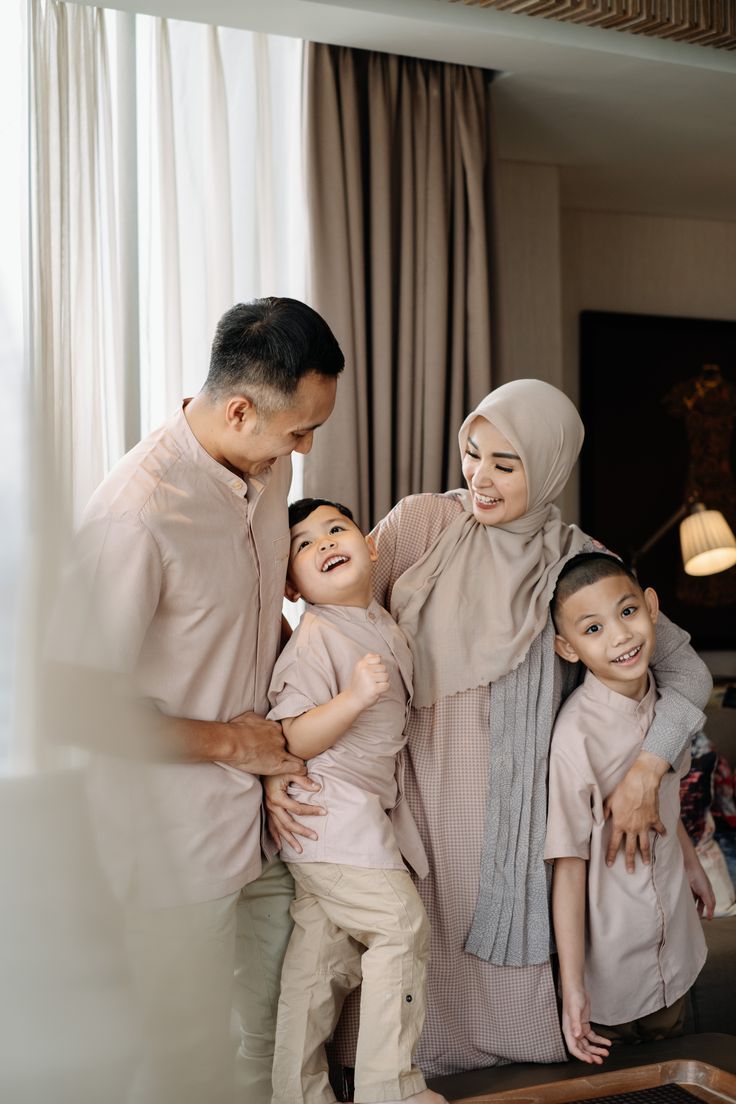 a man and two children standing next to each other in front of a window with curtains