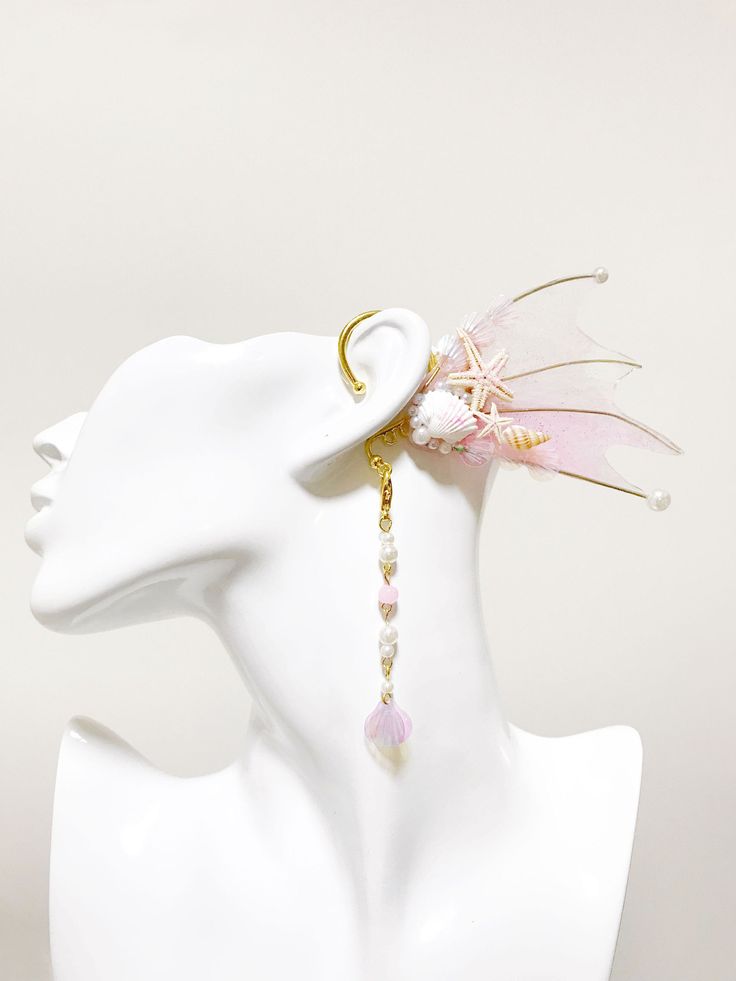 a white mannequin head with a pink and gold earring on top of it