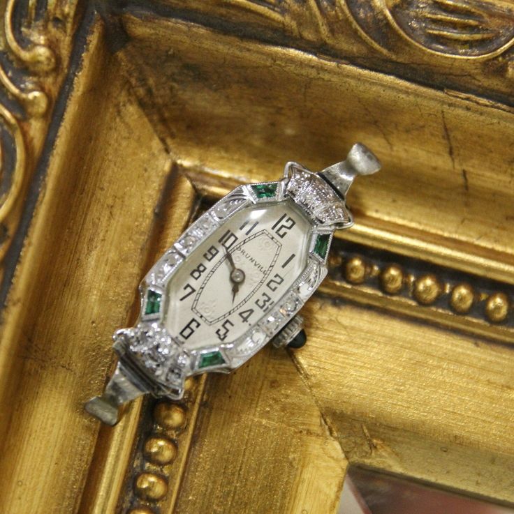 This is a beautifully crafted vintage 18K White Gold Jeweled Swiss made Art Deco watch. Elaborate detailing around the face. Emerald cabochon crown. The top and bottom synthetic emeralds on the left side are chipped, but this does not detract from the watch's overall beauty or functionality. This item is in good condition with only some wear, it has recently been professionally inspected and seems to be running normally. Please review the images provided. Please note, this does not include a ban Emerald Watch, Emerald Art Deco, Emerald Art, Art Deco Watch, Watch Women's, Vintage Watches Women, Watches Luxury, Jewelry Lockets, Watch Vintage