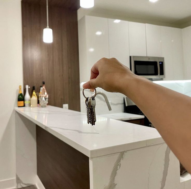 a hand holding a house key in front of a kitchen counter