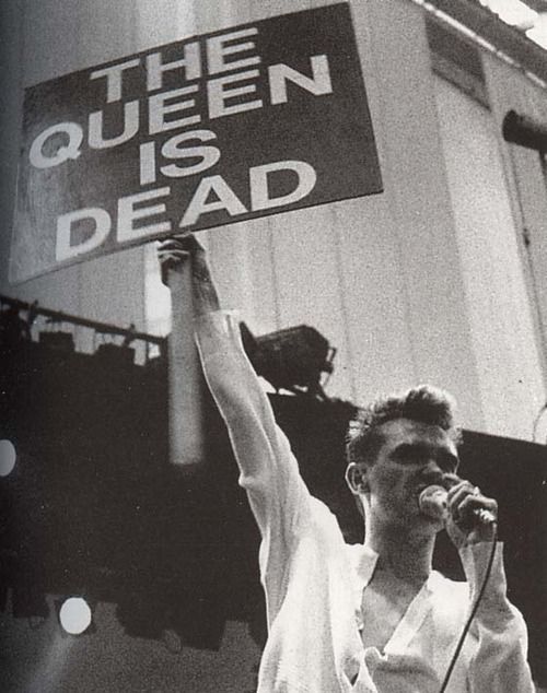 a man holding up a sign that says queen is dead