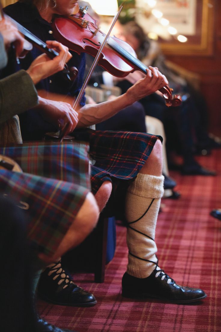 a woman playing the violin while sitting on a chair in front of other people wearing kilts