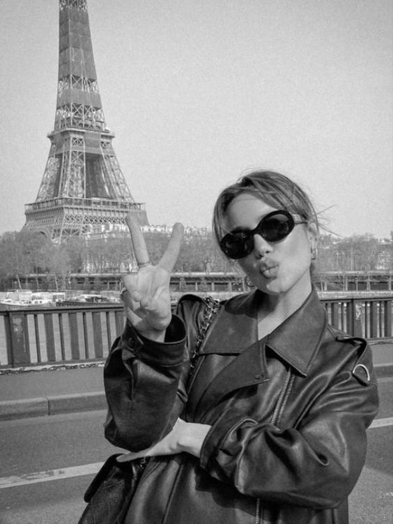 a woman in black jacket and sunglasses pointing at the camera with eiffel tower in background