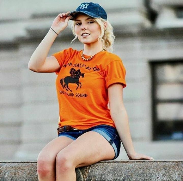 a woman in an orange shirt and blue shorts sitting on a wall with her legs crossed