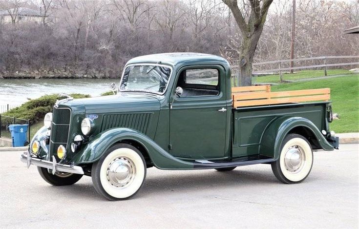 an old green truck parked in front of a tree with a bench on the back