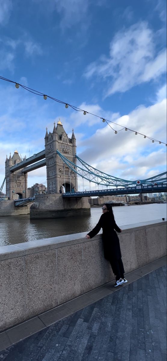 a person leaning against a wall in front of the tower bridge, with lights strung over it