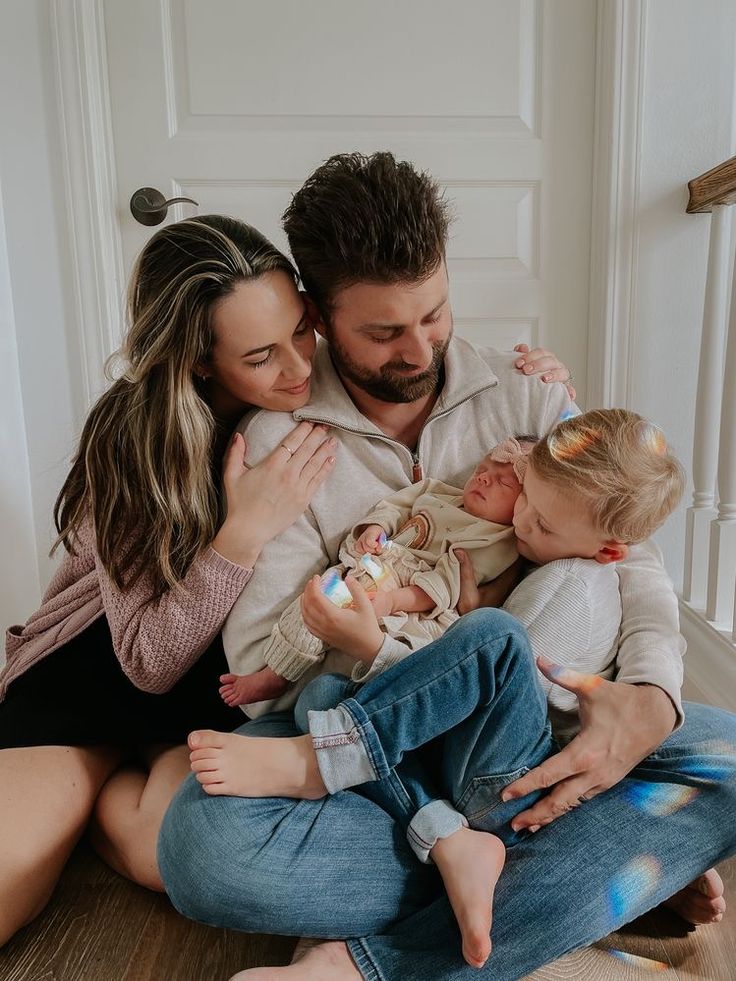 a man and woman sitting on the floor with their two babys in their arms