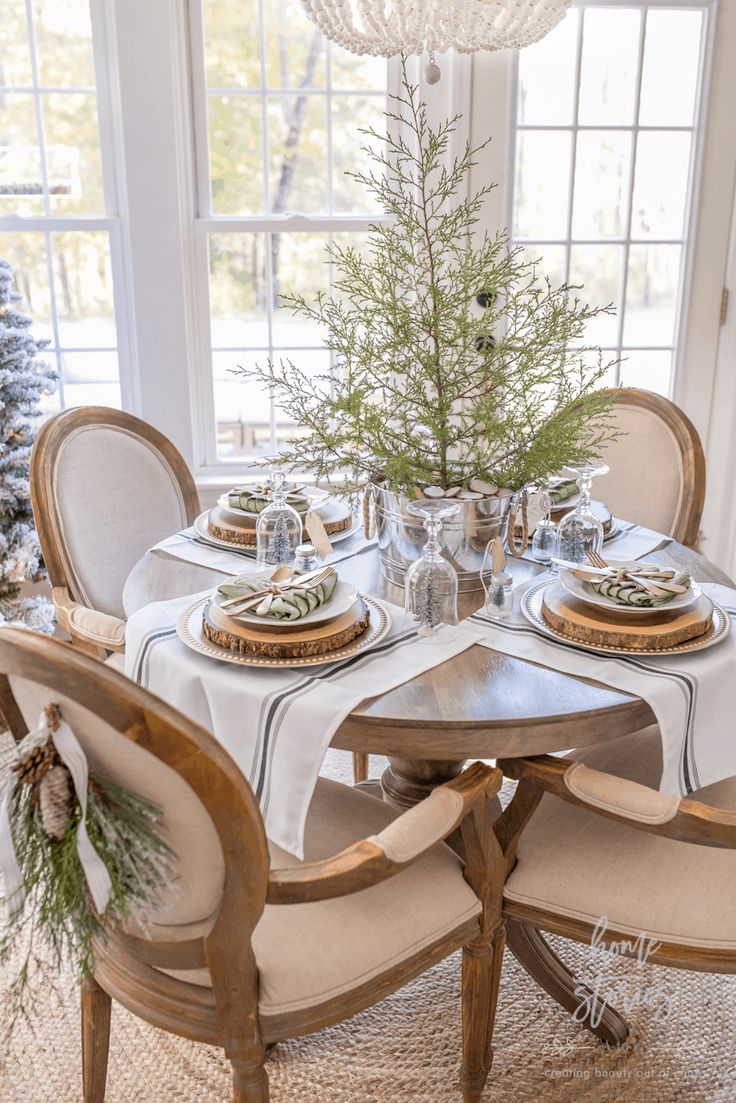 a dining room table set for christmas with white linens and greenery on top