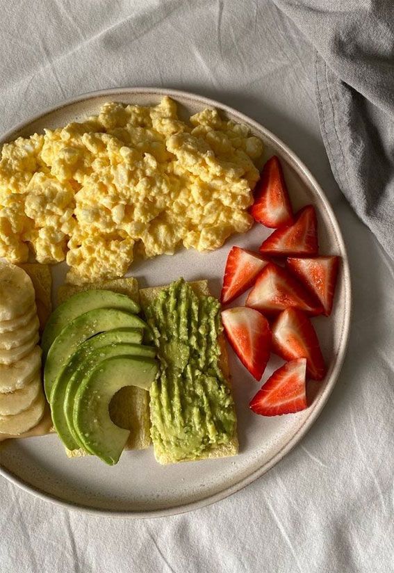 a white plate topped with eggs, fruit and crackers next to sliced strawberries