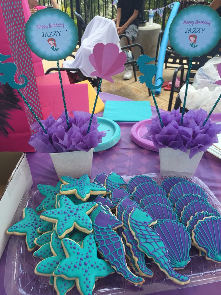 some decorated cookies are sitting on a purple table with pink and blue flowers in vases