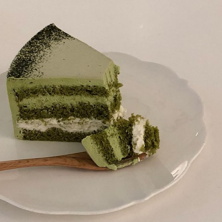 a piece of green cake on a white plate with a wooden spoon