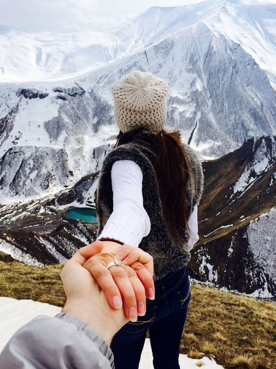 two people holding hands on top of a snow covered mountain with mountains in the background