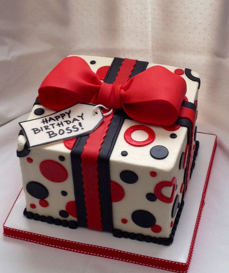 a birthday cake decorated with a gift box and red bow on it's side