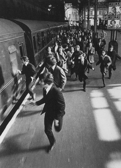 black and white photograph of people running on the train tracks in front of a subway car