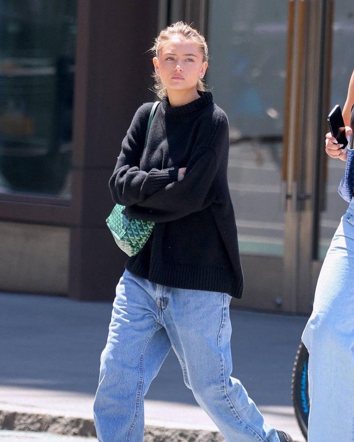 a woman in black sweater and jeans walking down the street with her hand on her hip