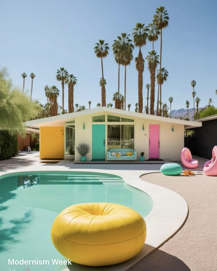 an outdoor pool with inflatable toys and palm trees around it, next to a house