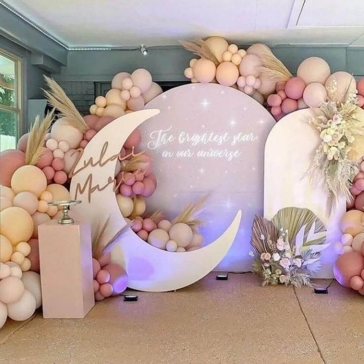 a decorated backdrop with balloons and flowers on the floor in front of a wall that says,