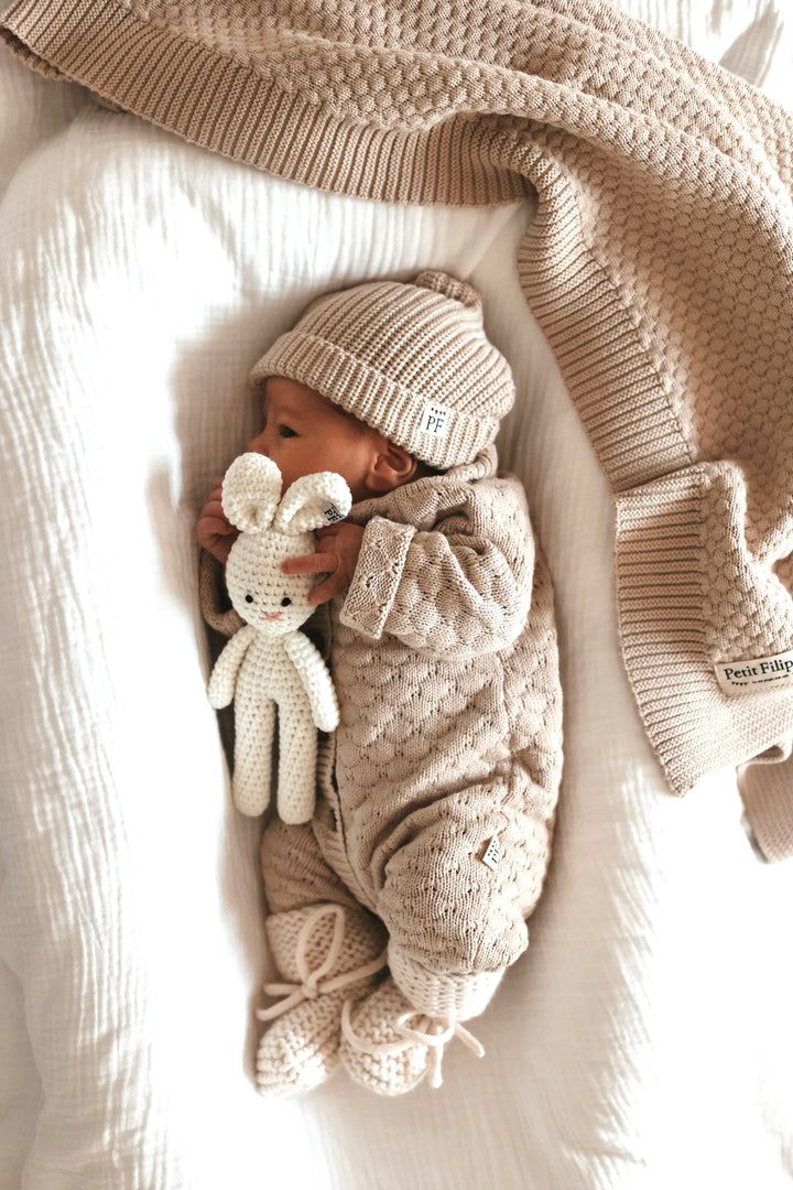 a baby is laying down with a stuffed animal in it's lap and wearing a knitted outfit