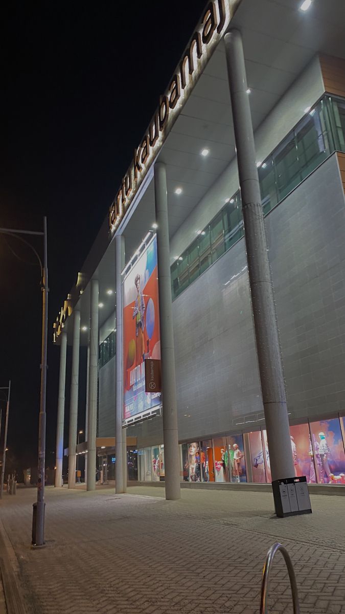 an empty street at night in front of a building with columns on the side and lights above it