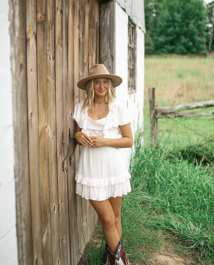 a woman wearing a hat leaning against a wooden fence in front of a barn door