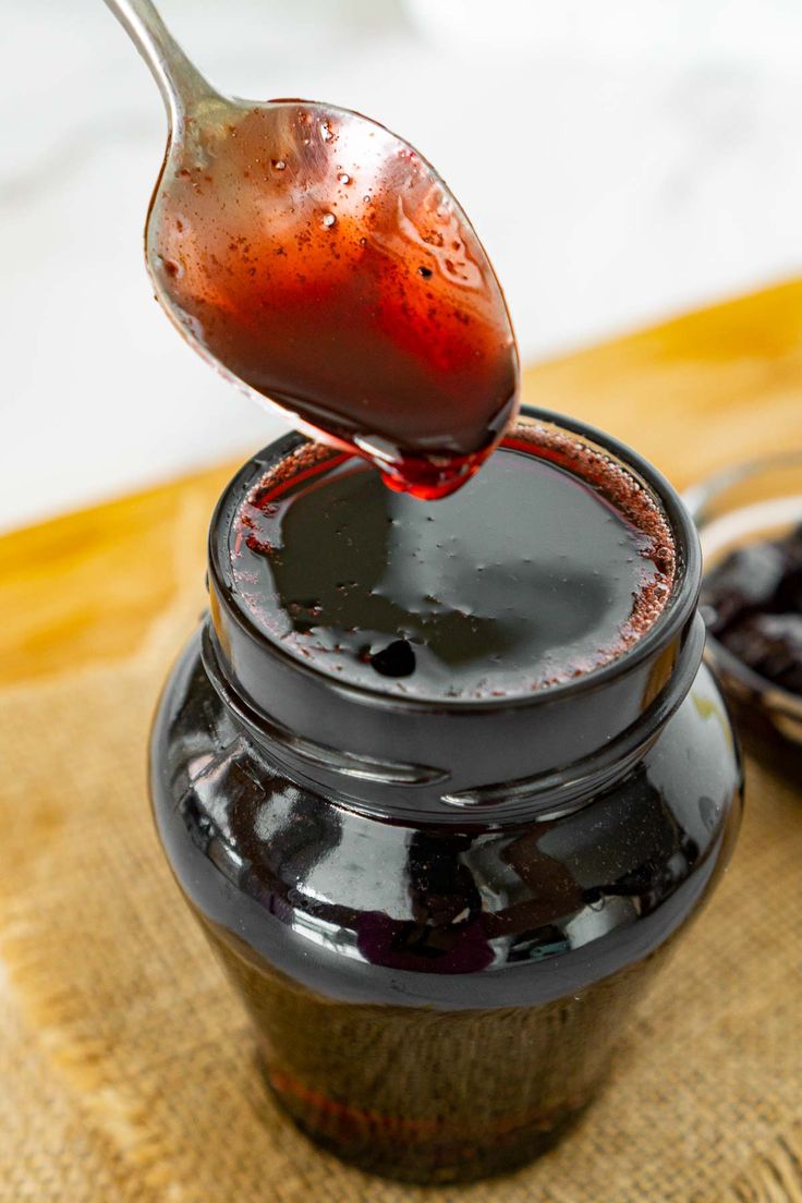 a spoon full of liquid sitting on top of a jar filled with blackberries and cherries